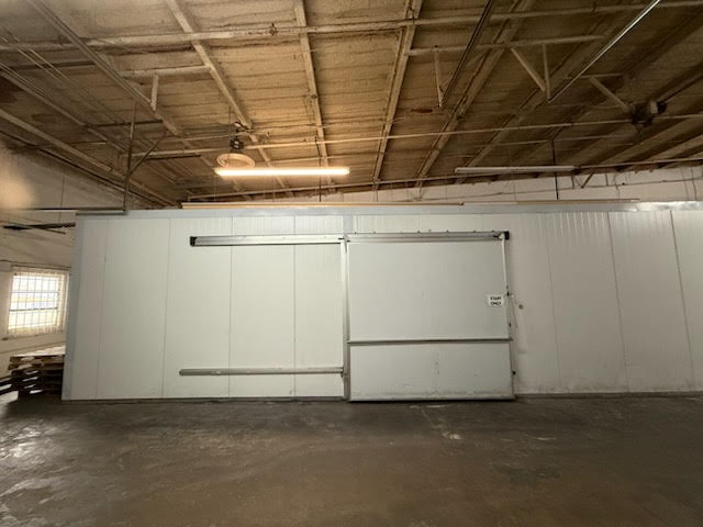 Industrial warehouse interior with a large white metal sliding door/partition and a high ceiling with exposed beams and a single fluorescent light.