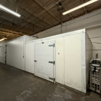 Industrial warehouse interior with white insulated storage rooms and a large metal door, under fluorescent lighting.