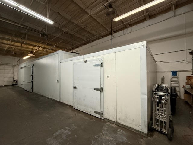 Industrial warehouse interior with white insulated storage rooms and a large metal door, under fluorescent lighting.